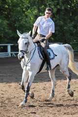 Jockey in glasses with whip riding horse on hippodrome