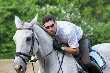 Jockey in glasses with whip hug horse on hippodrome