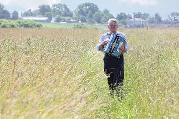 Grandfather plays accordion in field near village