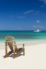 Fototapeta na wymiar Beach chair on sandy beach with white boat on background