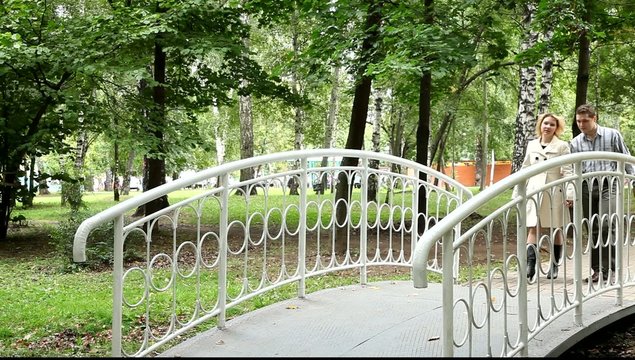 Двое влюблённых идут по мостику парка