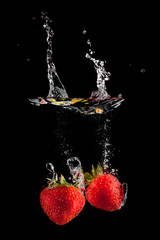 Two strawberries splashing on water