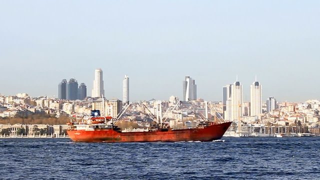 Red cargo ship sailing in front of the city