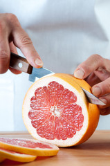 Vertical shot of a fresh grapefruit being sliced by female hands