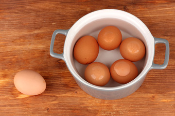 Boiled eggs in saucepan on wooden background