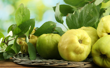 sweet quinces with leaves, on wooden table, on green background