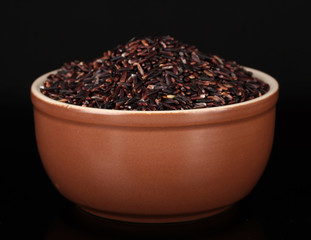 Black rice in brown bowl isolated on black