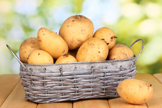 Ripe potatoes on basket on wooden table on natural background