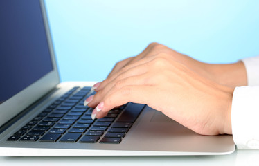 Hands typing on laptop keyboard close up on  blue background