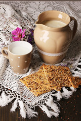 Pitcher and cup of milk with cookies on wooden table close-up
