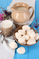 Pitcher and cup of milk with meringues on wooden table close-up