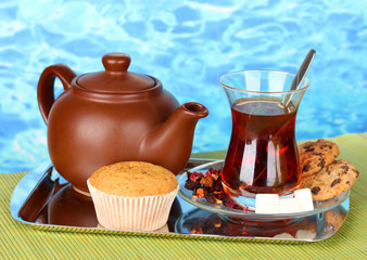 glass of Turkish tea and kettle on color background