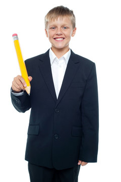 Cheerful young boy holding giant sized yellow pencil