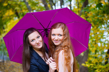 Two girls under umbrella in autumn park