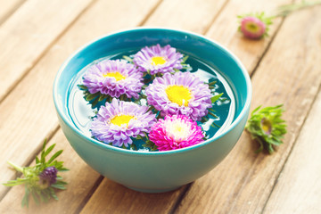 Aster flowers in bowl with water on wooden table. Spa concept.