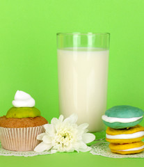 Glass of fresh new milk with cakes on green background