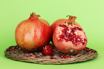 Ripe pomegranates on wicker cradle on green background