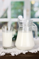 Pitcher and glass of milk on wooden table on window background