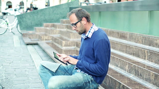 Young man with tablet computer sitting on the stairs, outdoors 