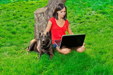 a girl with a notebook sitting under a tree together with a dog