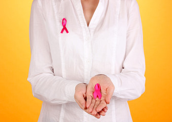 Woman with pink ribbon in hands on orange background