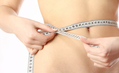 A female is measuring her waist whith measure tape