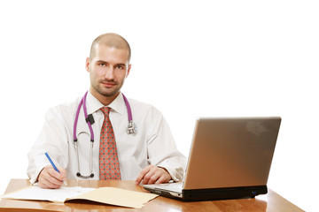 A male doctor is sitting and writing in front of a laptop