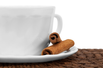 White cup with cinnamon, standing on coffee beans