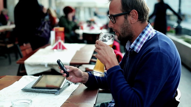 Young man with tablet and cellphone drinking beer