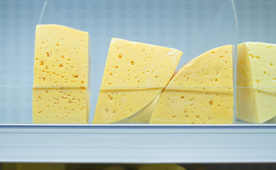 Round sectors and square cheese pieces on shelves in supermarket