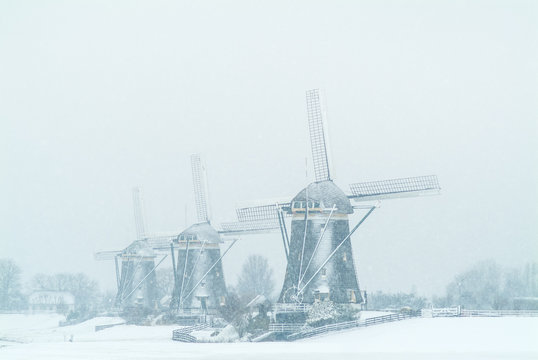 Three Dutch windmills during snowfall