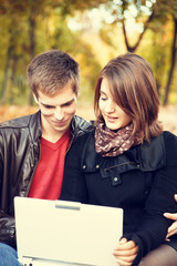 Beautiful couple with laptop at autumn park.