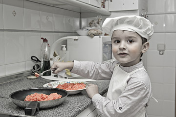 Un pequeño cocinero muy simpático y divertido en la cocina - obrazy, fototapety, plakaty