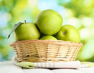 Ripe green apples with leaves in basket,