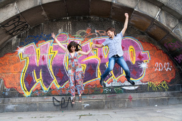 Couple jumping off the ledge with graffiti background