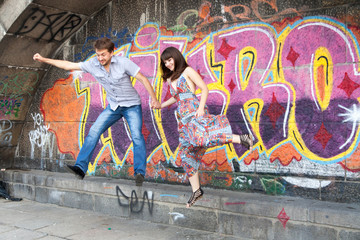 Obraz na płótnie Canvas Couple jumping off the ledge with graffiti background