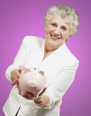 portrait of senior woman showing a piggy bank over pink backgrou