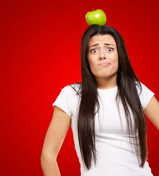 portrait of young woman holding green apple on her head over red