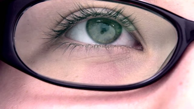 Extreme close up of an reading eye through the glasses.