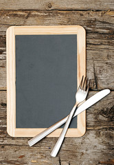 Menu blackboard lying on wooden table with knife and fork