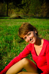 A young woman in a red sweater smiling sitting in autumn park