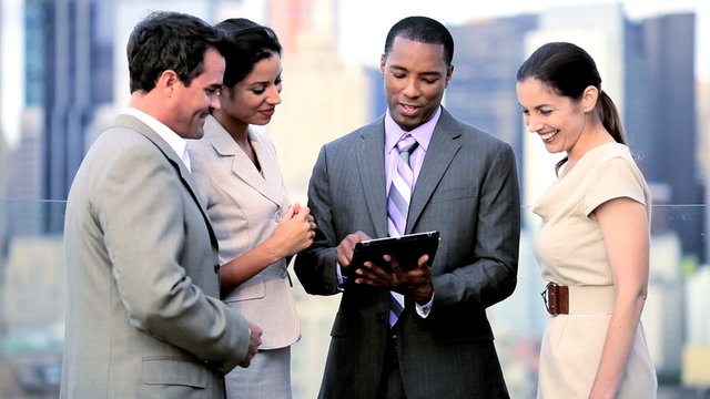 Multi ethnic management discussing data online on tablet on rooftop city office