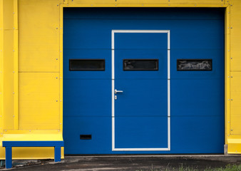 Obraz na płótnie Canvas Tekstura nowoczesną żółtej ścianie garażu przy zamkniętej bramie niebieskiej
