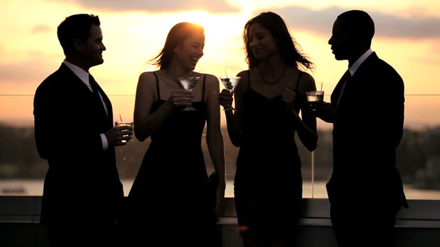 Multi ethnic friends laughing and drinking at luxury sunset roof cocktail party