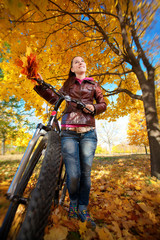 Naklejka premium woman with bike on a yellow autumn leafs background