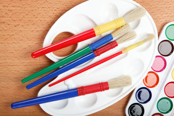 Paint, palette and brushes on a wooden table.