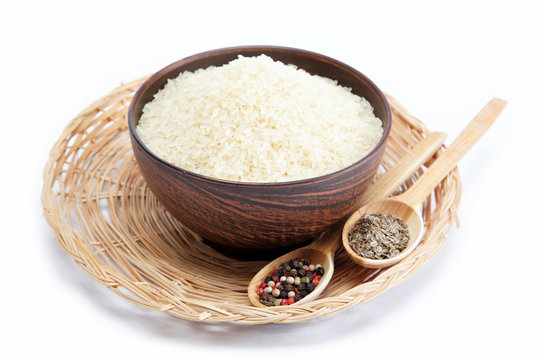 Grains of rice in a bowl and two wooden spoons with spices isola