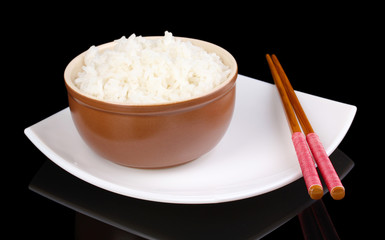 Bowl of rice and chopsticks on plate isolated on black