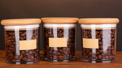 Coffee beans in jars on table on brown background