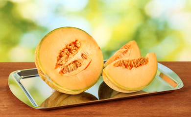 Cut melon on metal tray on green background close-up